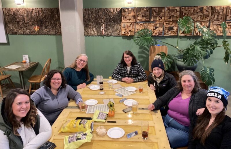 A group of women smiles at the camera. They are sitting inside Earthen Ales brewery in Traverse City.