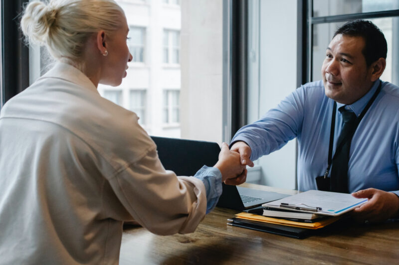 Two people shake hands across a desk.