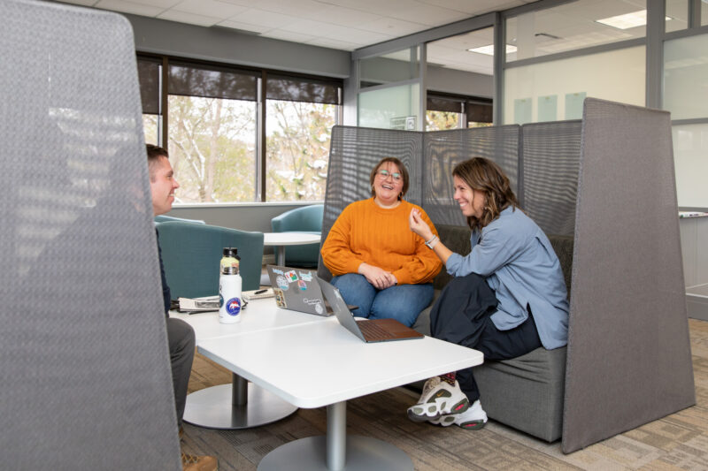 Three young workers laugh while having a discussing sitting in a booth at the 20Fathoms office.