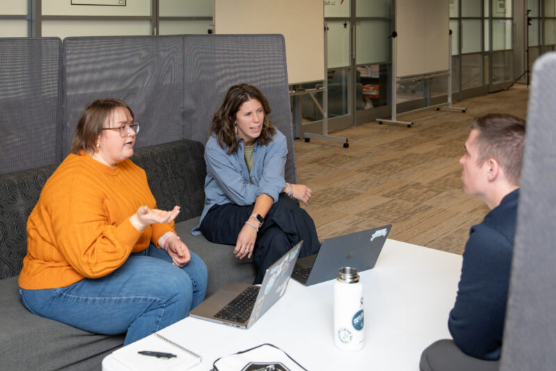 A group of coworkers discuss something intently while sitting in a shared booth.